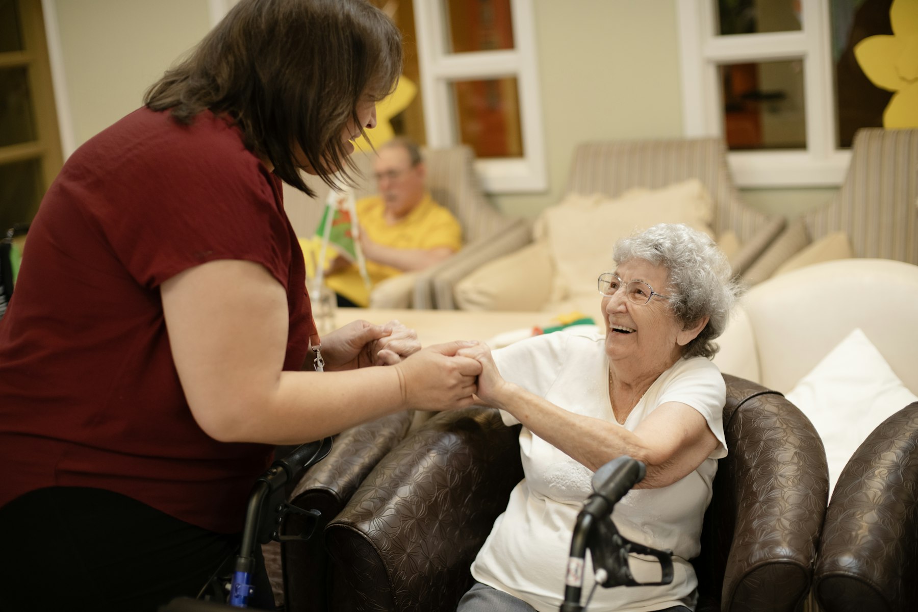 A caregiver holding hands with a smiling resident in a care home lounge